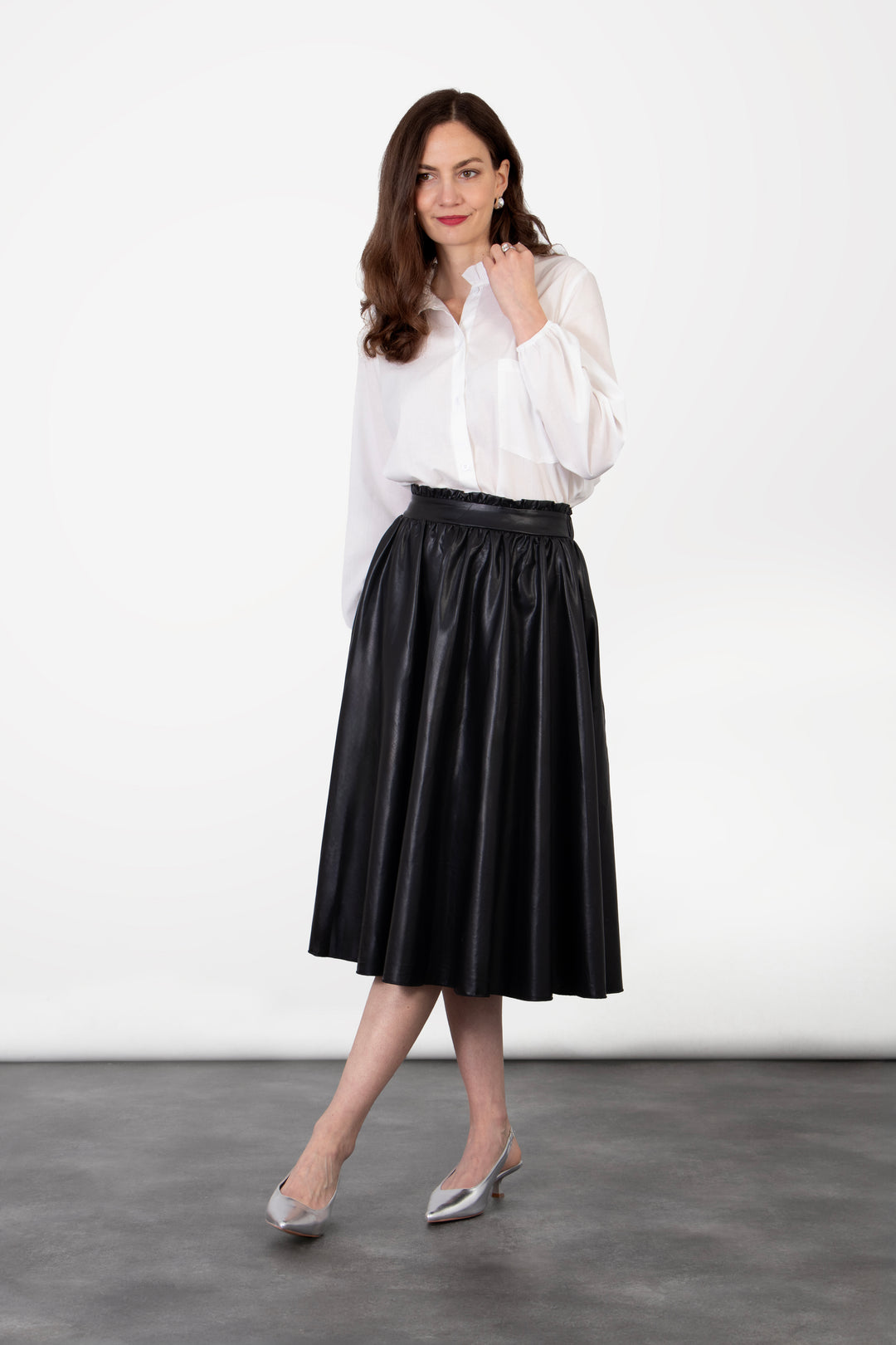 model wearing a plain black faux leather ruffled midi skirt, the skirt is a-line in shape