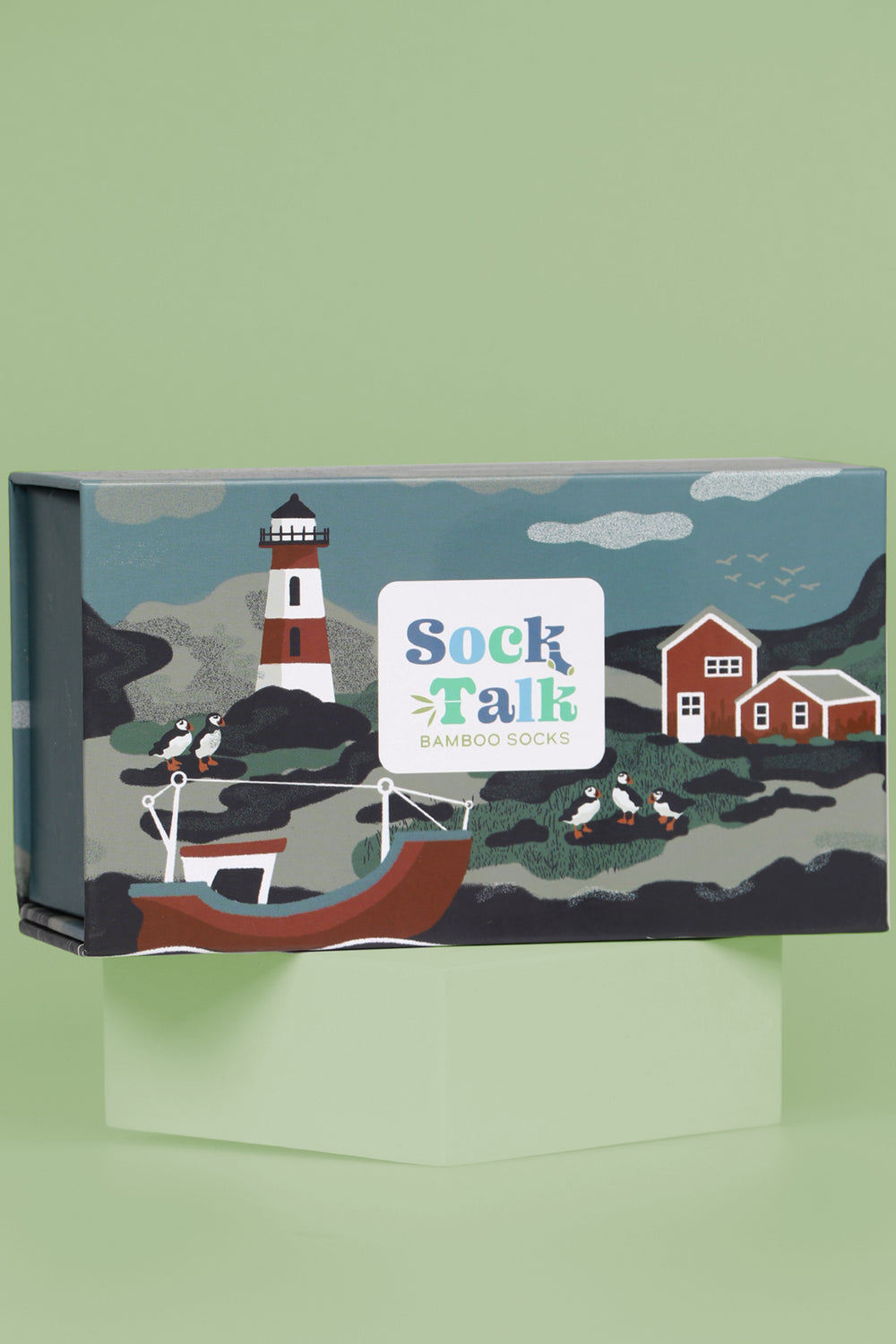 close up of the gift box, it is designed to look like a scenic fishing village with a lighthouse, fishing boats and puffins sitting on rocks