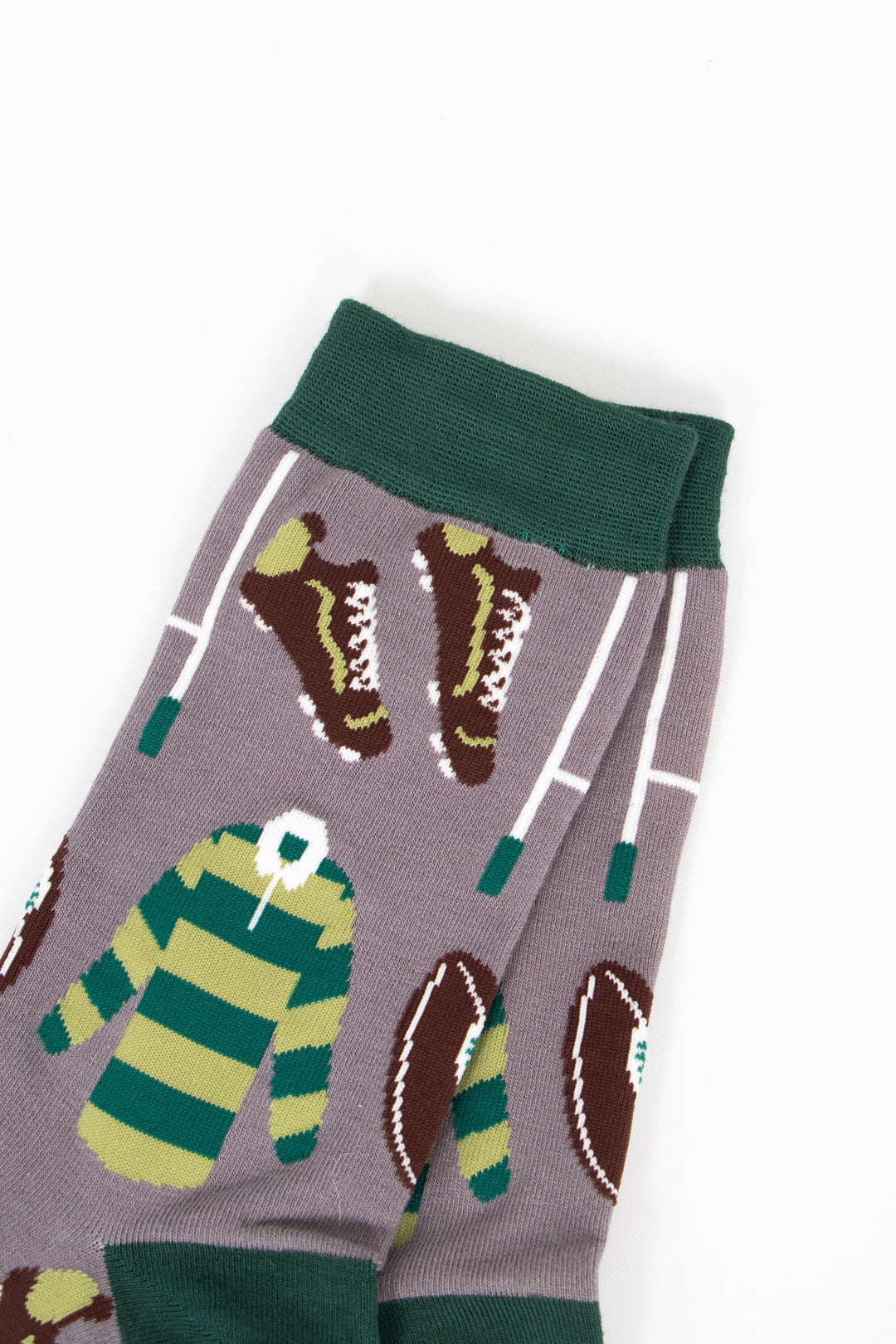 close up of the rugby inspired design. there are brown rugby boots with white studs and white laces, white goal posts and a light and dark green striped rugby shirt with a contrasting white collar. this pattern is repeated all over the design.