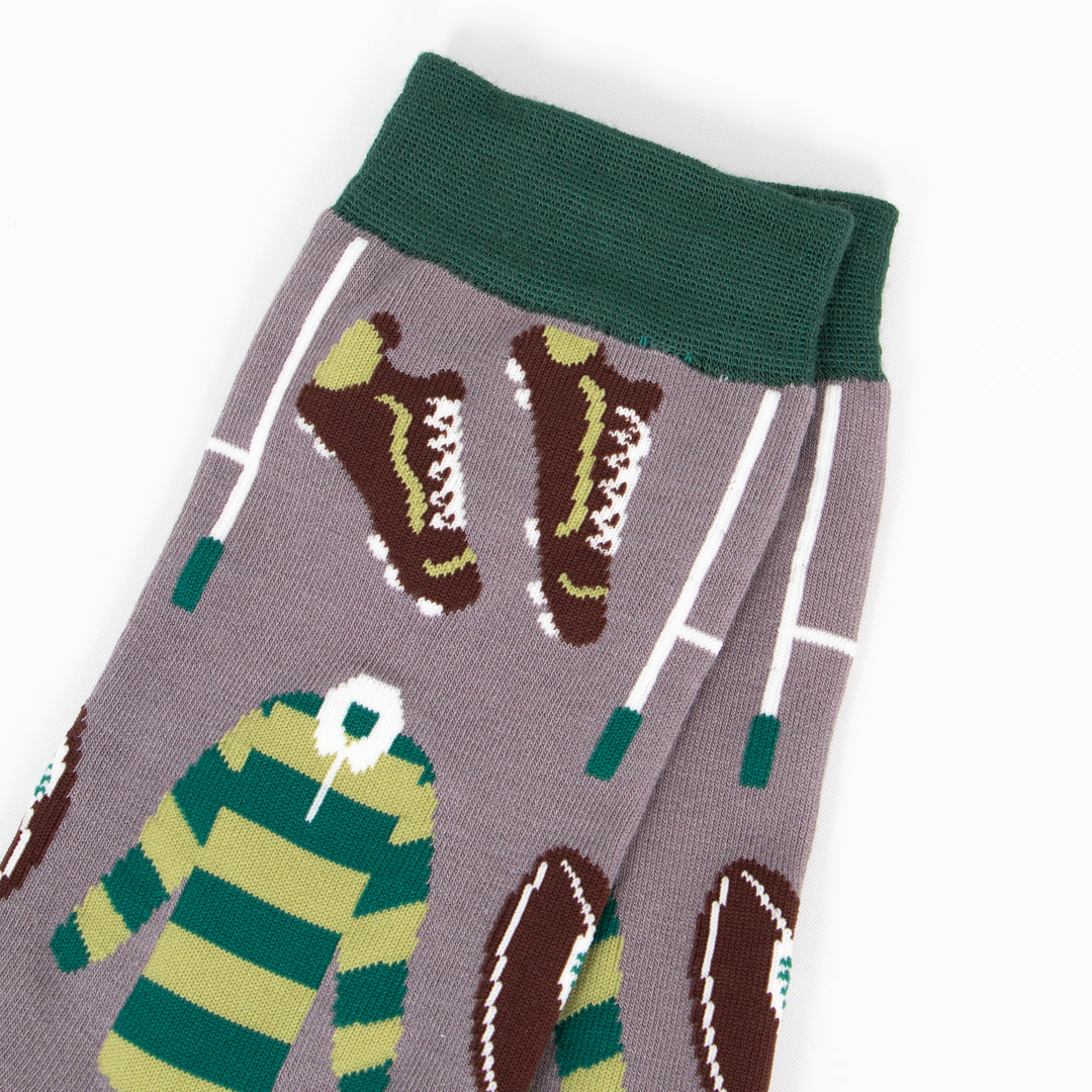 close up of the rugby inspired design. there are brown rugby boots with white studs and white laces, white goal posts and a light and dark green striped rugby shirt with a contrasting white collar. this pattern is repeated all over the design.