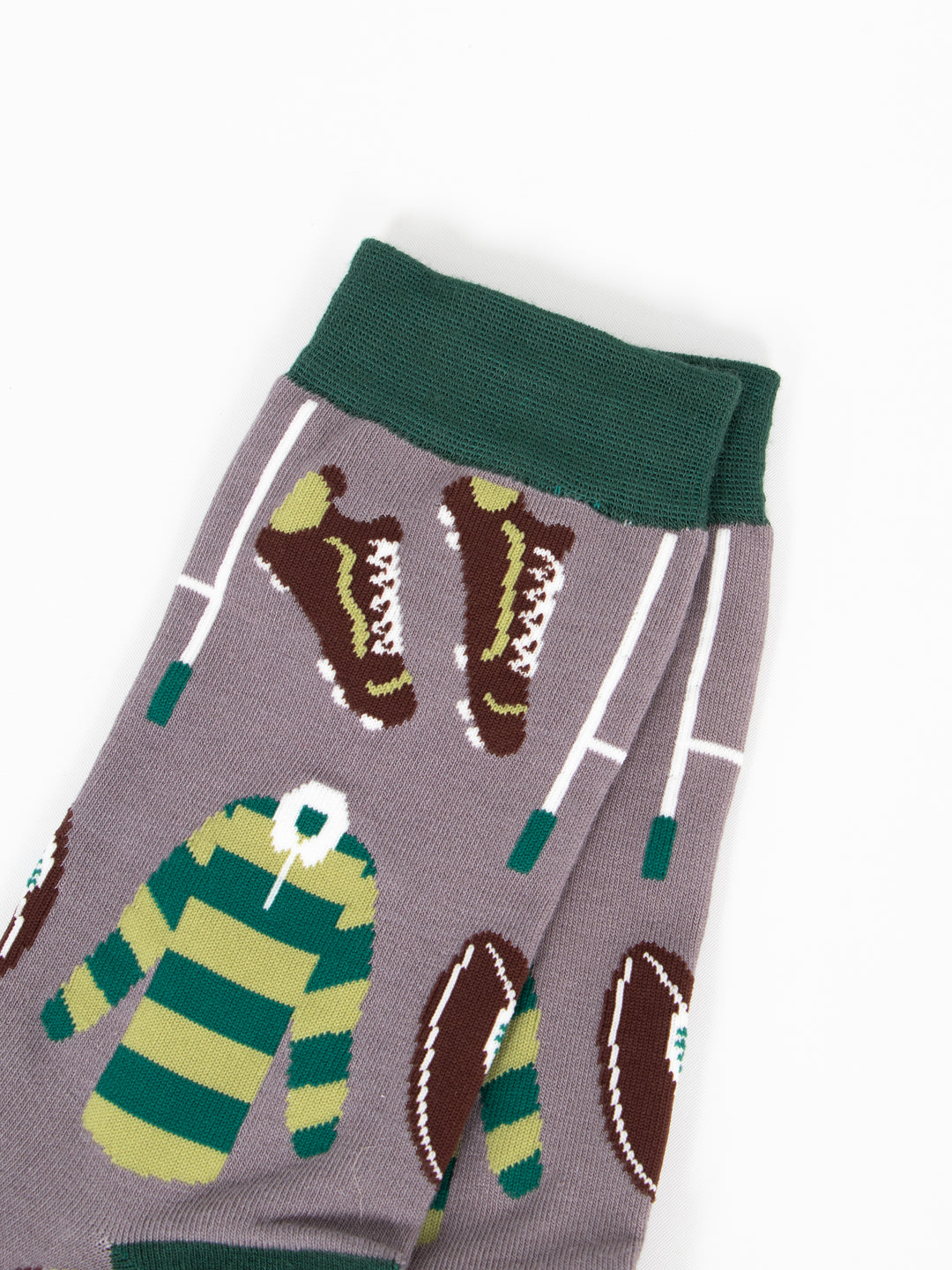 close up of the rugby inspired design. there are brown rugby boots with white studs and white laces, white goal posts and a light and dark green striped rugby shirt with a contrasting white collar. this pattern is repeated all over the design.