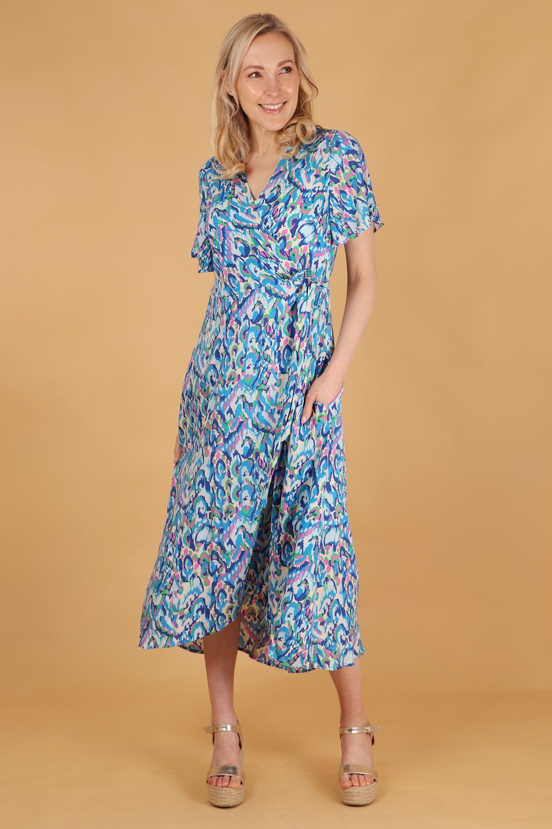 model wearing a blue and pink abstract pattern midi wrap dress with short sleeves, v-neck and waist tie