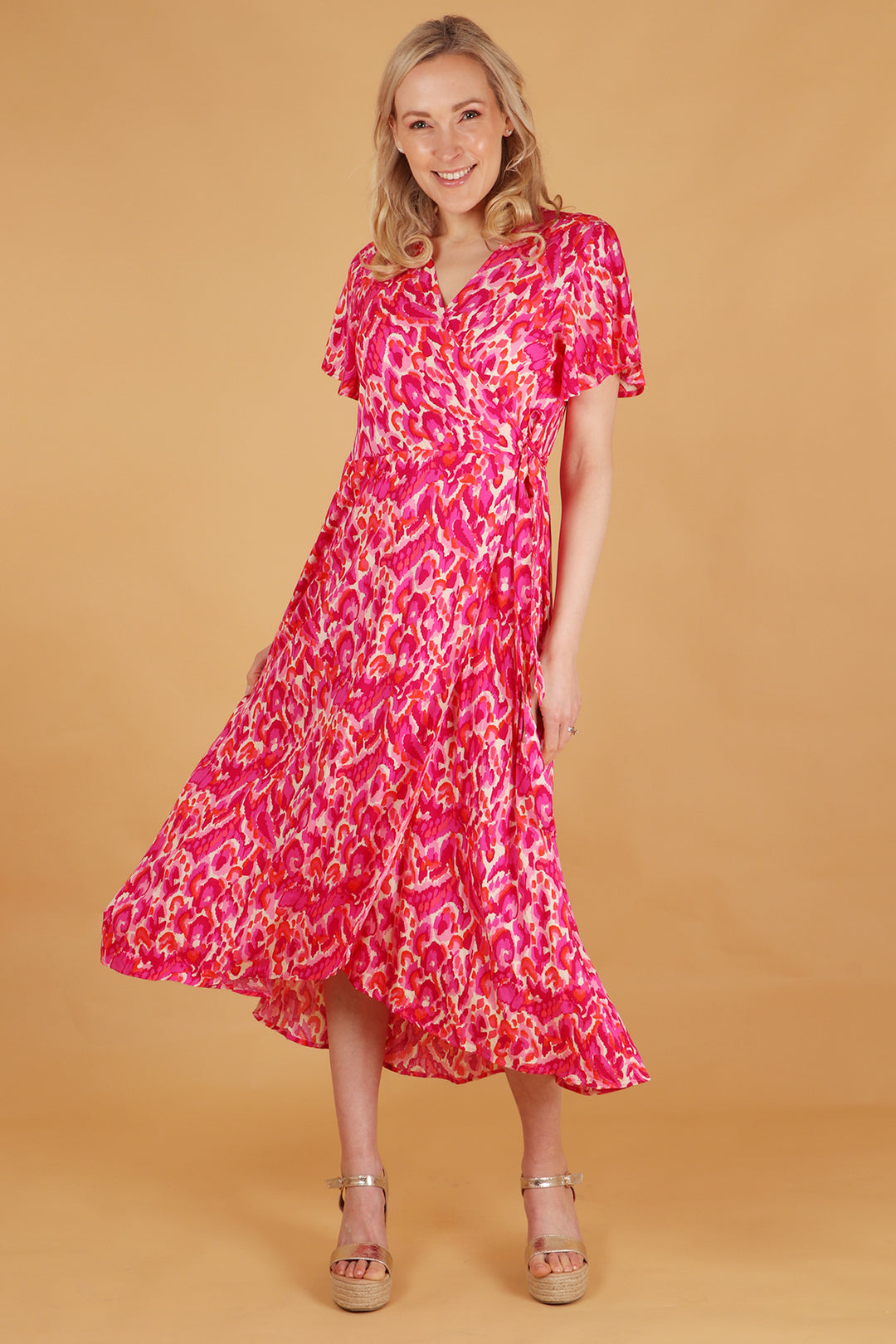 model wearing a pink abstract pattern midi wrap dress with short sleeves, v-neck and waist tie