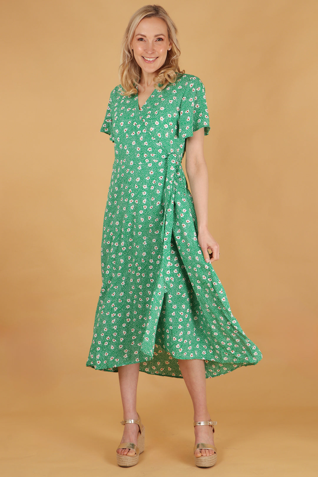 model wearing a green midi length wrap dress with an all over white daisy floral pattern. the dress has short sleeves, waist tie and vneck