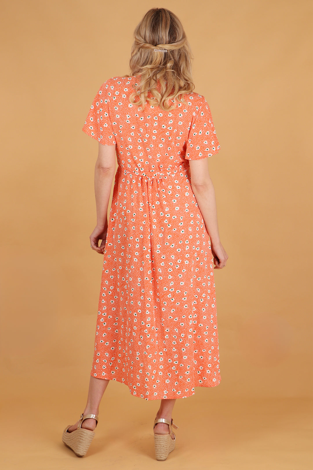 model showing the back of the orange daisy print dress showing an all over pattern